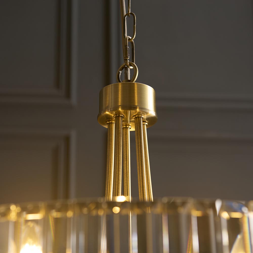 Fairfax 5 Light Pendant in antique brass, close-up of chain link, brass canopy and rods above faceted glass, set against a dark panelled wall.