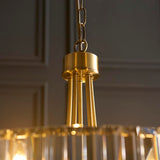 Fairfax 5 Light Pendant in antique brass, close-up of chain link, brass canopy and rods above faceted glass, set against a dark panelled wall.