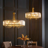 Fairfax 5 Light Pendant in antique brass with round crystal glass shade, shown above a dining table in a dark panelled room alongside a second matching fixture.