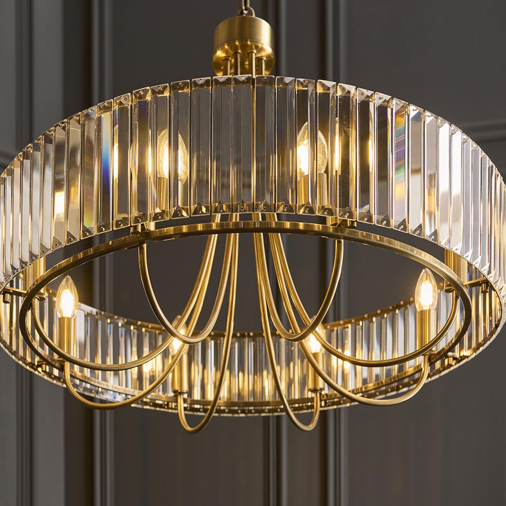 Endon Fairfax 8 Light Pendant in antique brass with a circular frame of clear cut lozenge glass and lit E14 lamps, shown against a dark grey wall.