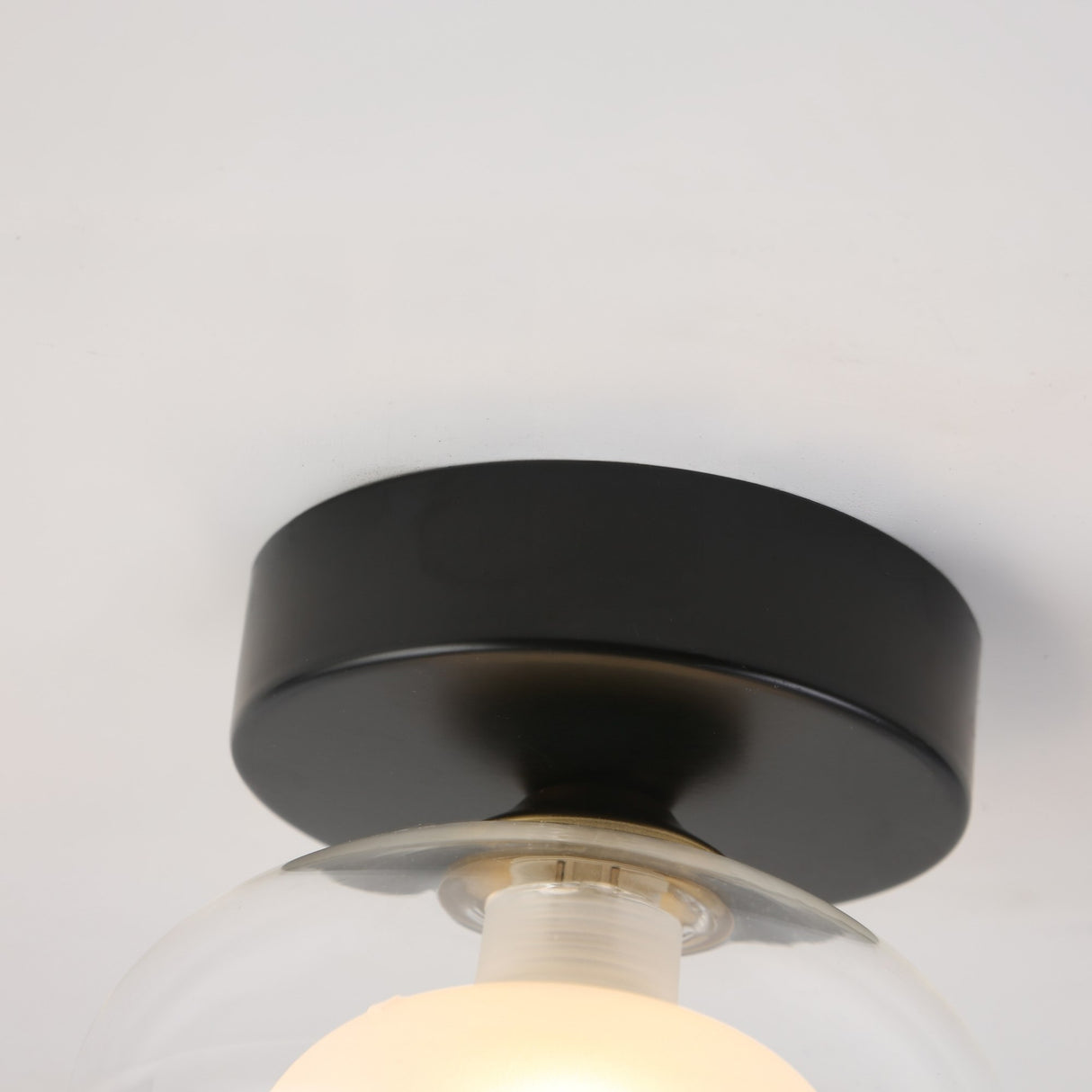 Close-up of the retro Galaxy 1 Light Wall/Flush Ceiling Light in black & white, showcasing its glowing bulb under a glass cover, mounted on a white ceiling.