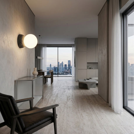 Minimalist apartment with light wood floors, neutral walls, modern black chair, Origo Concrete Wall Light in black & white, and large windows framing a city skyline. Simple décor gives the space an airy, uncluttered feel.