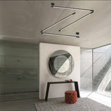 Index 1 Light Cylinder Ceiling Light in matte black metal, angular multi-arm LED design mounted on a concrete ceiling above a round mirror and console table.