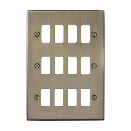 12 Gang Square Edge Grid Switch Plate in antique brass, rectangular metal faceplate with twelve openings in three rows of four and four fixing screws, on a white background.