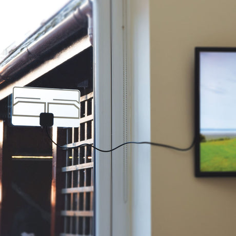AVSL Mercury ST25P paper-thin transparent indoor TV aerial fixed to a window with black coaxial lead running along the wall to a framed picture.