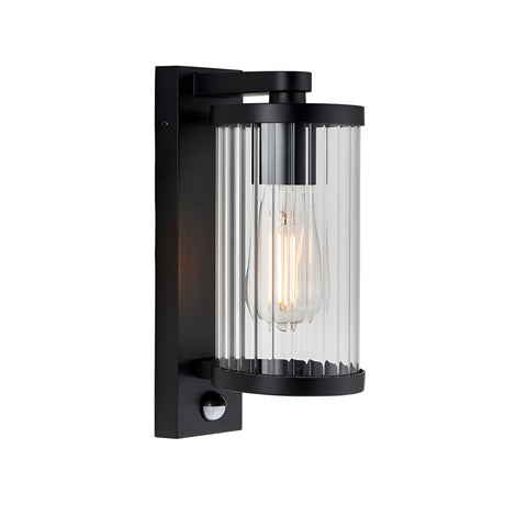 Endon Castbury outdoor wall light in matt black with a cylindrical ribbed glass shade, E27 filament bulb and integrated PIR sensor below.