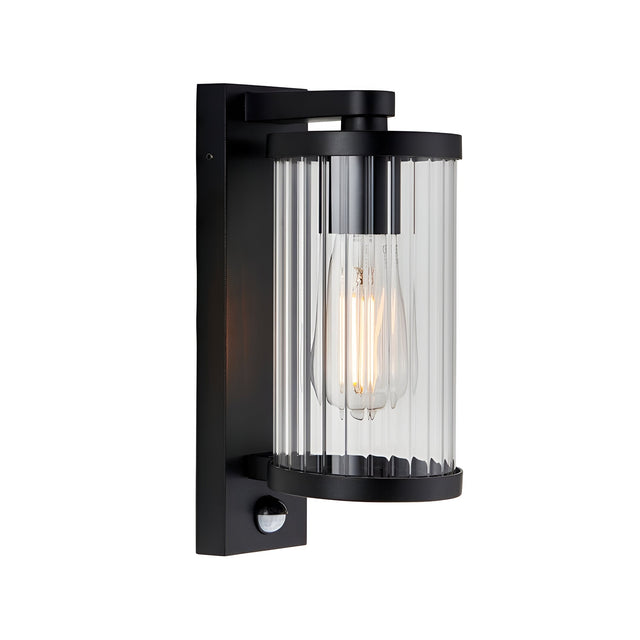 Endon Castbury outdoor wall light in matt black with a cylindrical ribbed glass shade, E27 filament bulb and integrated PIR sensor below.