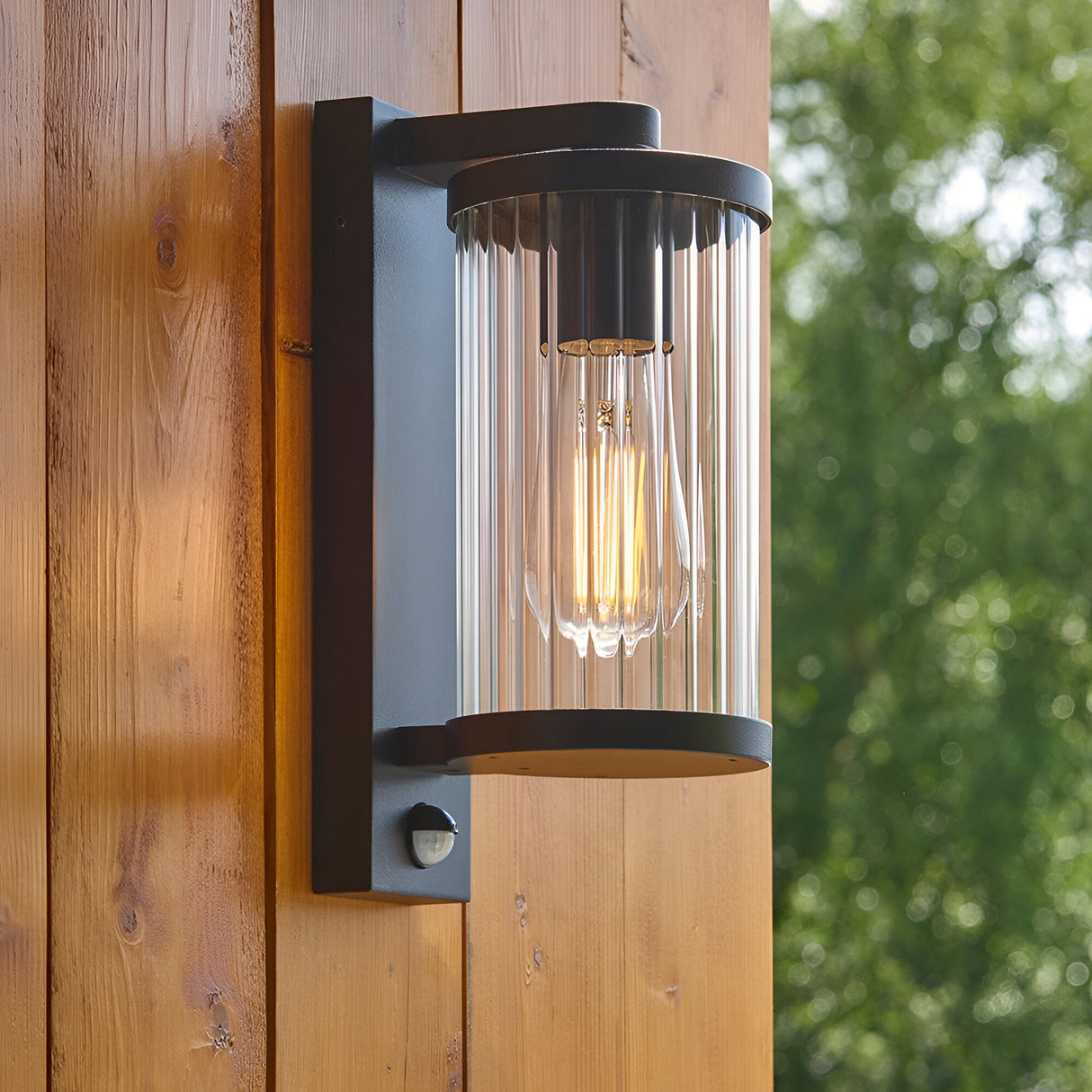 Endon Castbury outdoor wall light in matt black with clear ribbed glass shade, E27 filament bulb and PIR sensor, mounted on a timber wall.