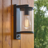Endon Castbury outdoor wall light in matt black with clear ribbed glass shade, E27 filament bulb and PIR sensor, mounted on a timber wall.
