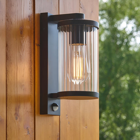 Endon Castbury outdoor wall light in matt black with clear ribbed glass shade, E27 filament bulb and PIR sensor, mounted on a timber wall.