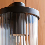 Close-up of Endon Castbury outdoor wall light showing the matt black cylindrical top and clear ribbed glass shade mounted on a timber wall.