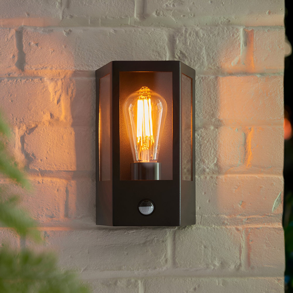 Brenshaw Outdoor Wall Light in matt black with a cubed glass panel frame, built-in PIR sensor, and E27 bulb, mounted on a brick wall.