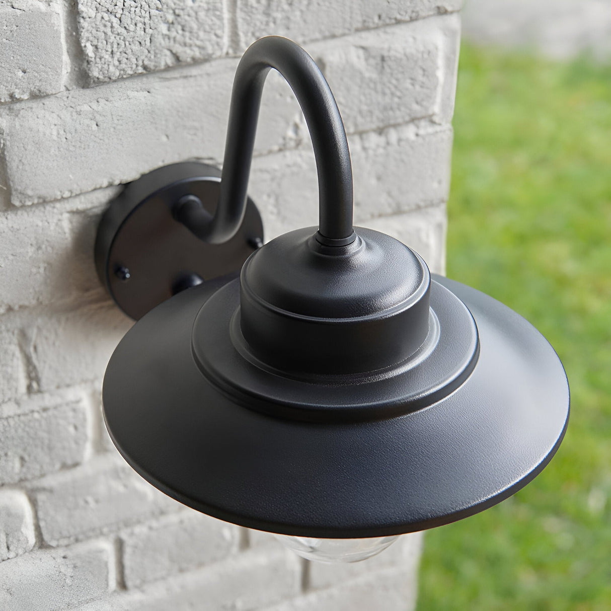 Endon Cranhurst outdoor wall light in matt black with a curved arm, wide-brimmed shade and clear glass dome, mounted on a white brick wall.