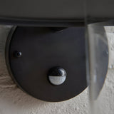 Close-up of the Endon Cranhurst outdoor wall light in matt black, showing the integrated PIR motion sensor beneath the curved shade on a textured wall.
