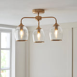 Halstead 3 Light Semi-Flush Ceiling Light in aged brass with clear glass shades and exposed bulbs, shown fitted in a white-walled room.