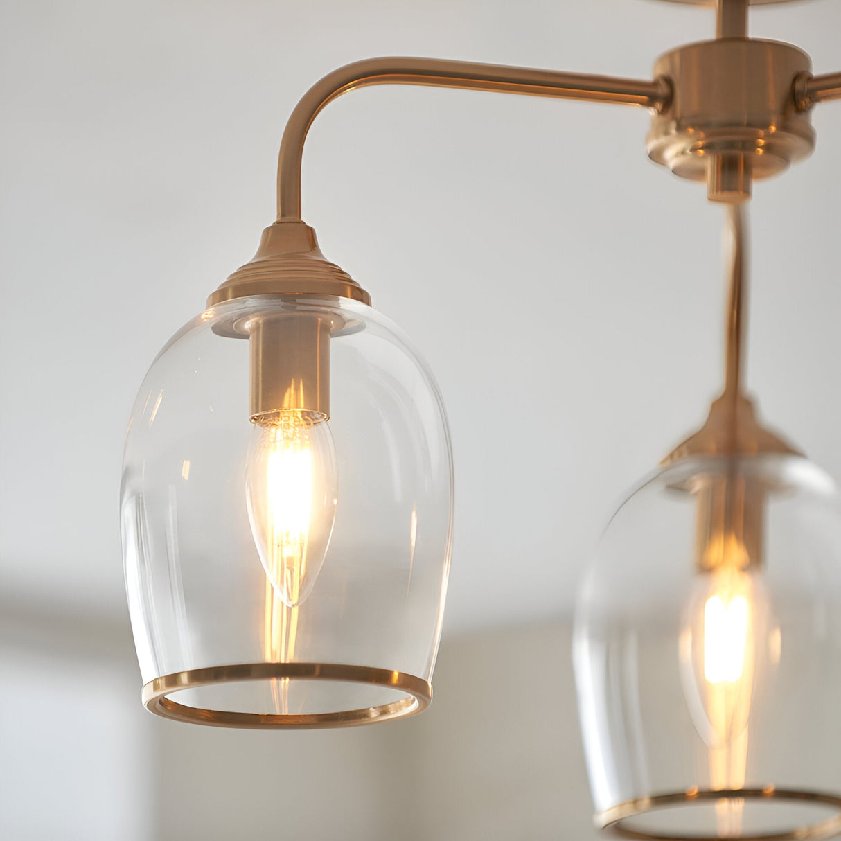 Halstead 3 Light Semi-Flush Ceiling Light in aged brass, close-up of curved brass arms holding clear glass shades with visible E14 bulbs, light grey background.