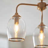 Halstead 3 Light Semi-Flush Ceiling Light in aged brass, close-up of curved brass arms holding clear glass shades with visible E14 bulbs, light grey background.