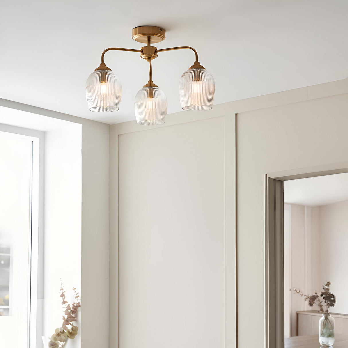 Endon Halstead Ribbed 3 light semi-flush ceiling light in aged brass with ribbed glass shades, installed in a neutral hallway with a mirror and window.