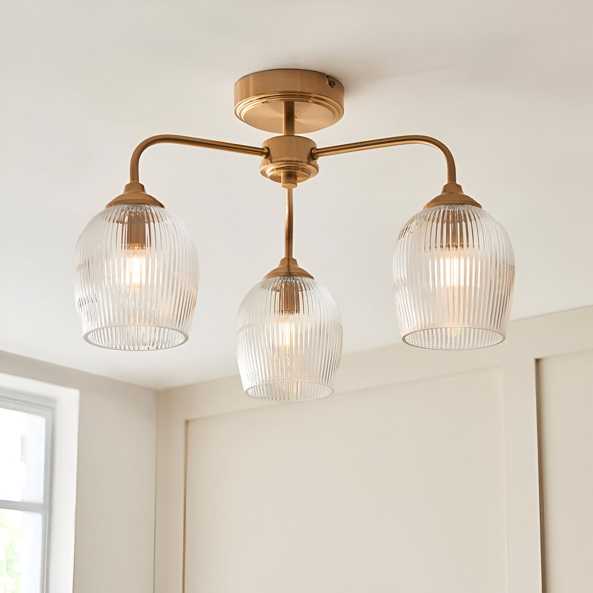 Endon Halstead Ribbed 3 light semi-flush ceiling light in aged brass with three ribbed glass shades on curved arms, shown on a white ceiling.