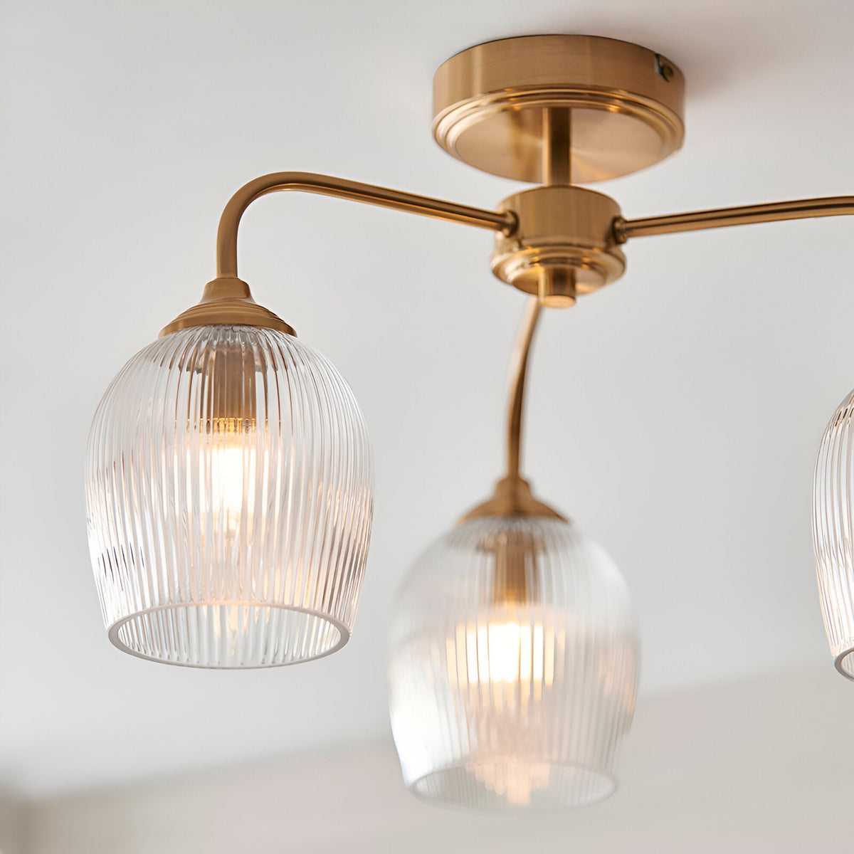 Endon Halstead Ribbed 3 light semi-flush ceiling light in aged brass, with curved arms and ribbed glass dome shades illuminated warmly.