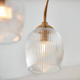 Close-up of Endon Halstead Ribbed semi-flush ceiling light shade in aged brass, showing a ribbed glass dome lit by a warm E14 bulb on a curved arm.