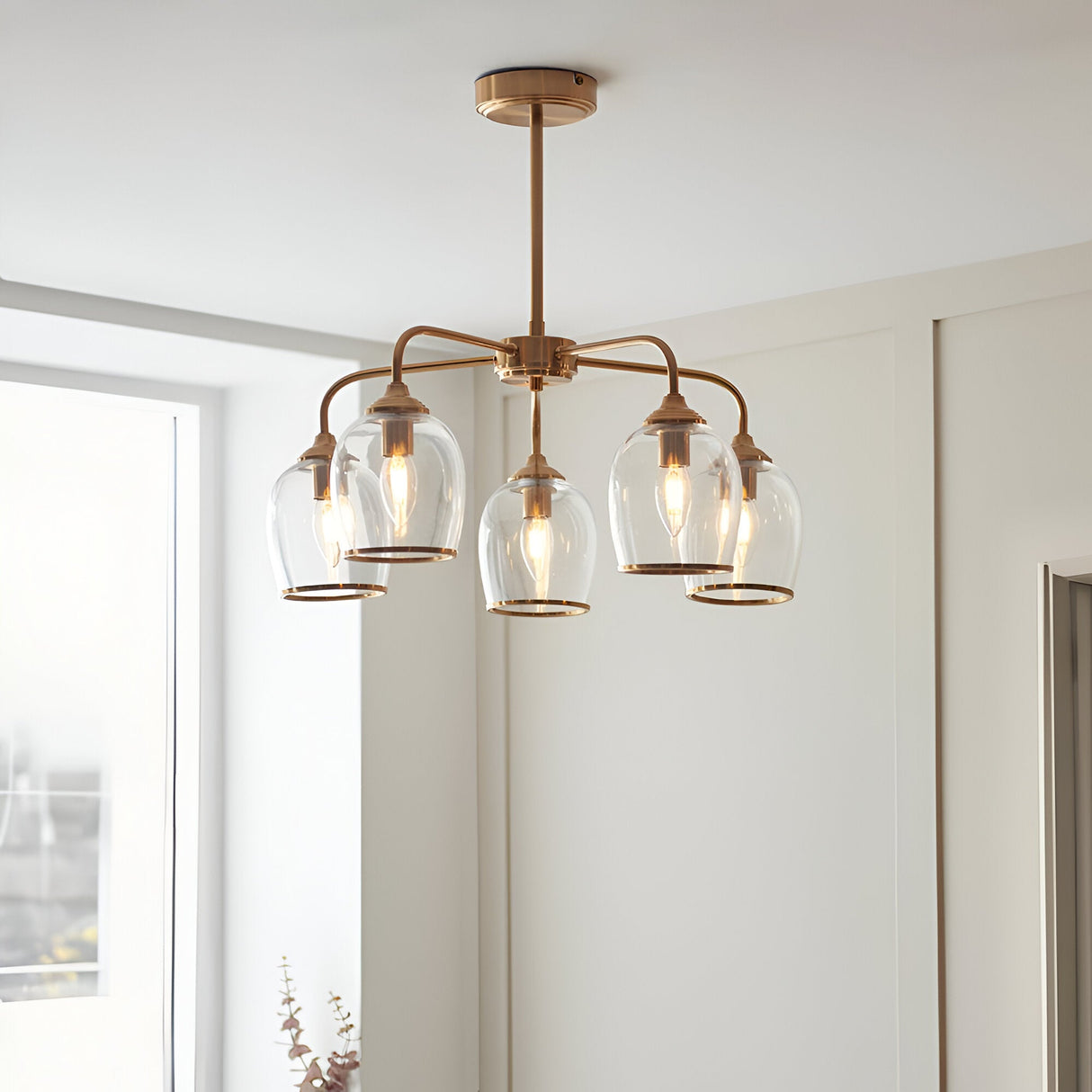 Halstead 5 Light Pendant in brass with arched arms and clear glass shades edged in metal trim, shown with filament bulbs in a room setting.