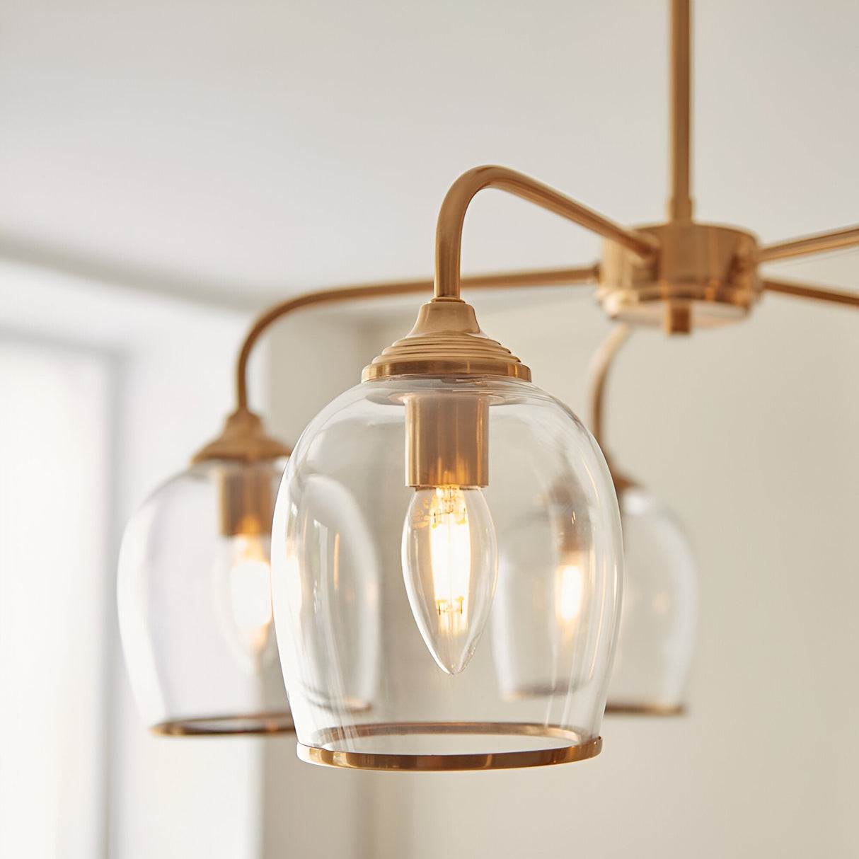 Halstead 5 Light Pendant in brass, arched arms holding clear glass shades with metal trim and visible filament bulbs, close-up view.