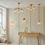 Halstead 5 Light Pendant in brass with arched arms and clear glass shades, shown in a living room alongside matching wall and floor lights.