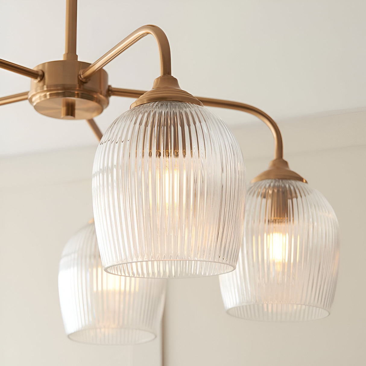 Endon Halstead five-light semi-flush pendant in brushed brass with curved arms and fluted clear glass shades, shown close-up against a pale ceiling.