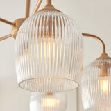 Close-up of Endon Halstead Ribbed 5 Light Pendant in brass, showing fluted clear glass shades on curved arms with warm filament lamps glowing.