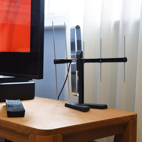 AVSL Mercury ST02 UHF indoor TV aerial with double reflector and black base, set on a wooden table beside a TV and remote near a curtained window.