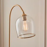 Halstead Floor Lamp in aged brass, close-up of the curved stem and domed clear glass shade with brass rim framing a filament bulb.