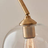Halstead Floor Lamp in aged brass, close-up of the curved stem and ribbed fitting holding a clear domed glass shade with visible filament bulb.