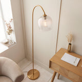 Endon Halstead floor lamp with an arched aged brass stem and ribbed domed glass shade, styled in a neutral reading nook beside a wooden side table.