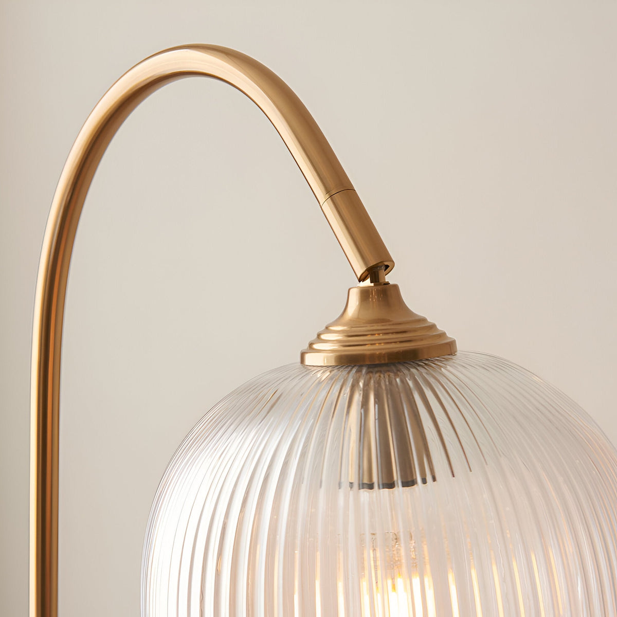 Close-up of the Endon Halstead floor lamp's curved aged brass stem and adjustable head above a ribbed domed clear glass shade.