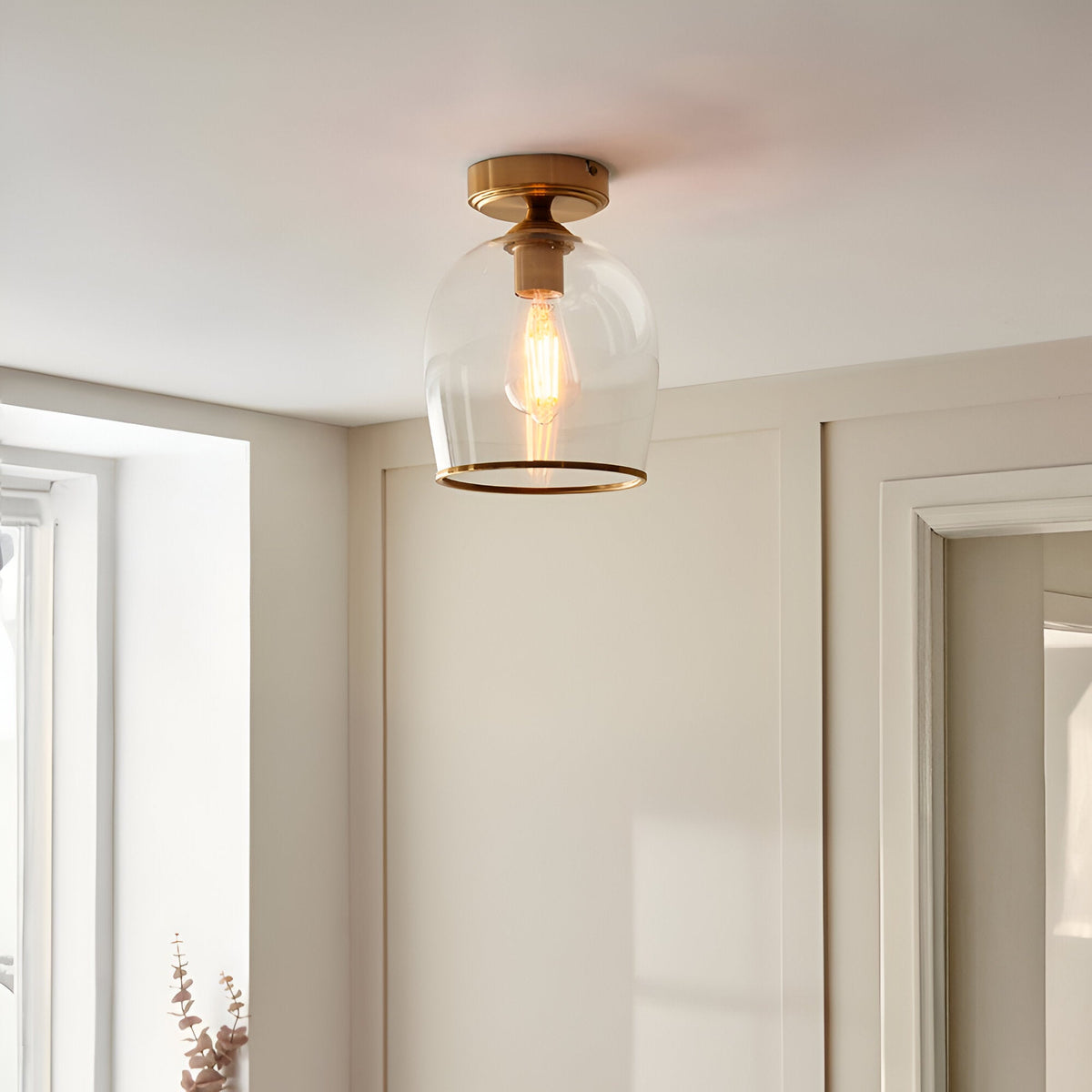 Halstead Flush Ceiling Light in aged brass with clear glass shade and exposed bulb, shown fitted in a hallway ceiling.