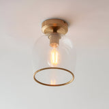 Halstead flush ceiling light in aged brass with clear glass bell shade, ring detail and visible E27 filament bulb, shown against a plain white background.