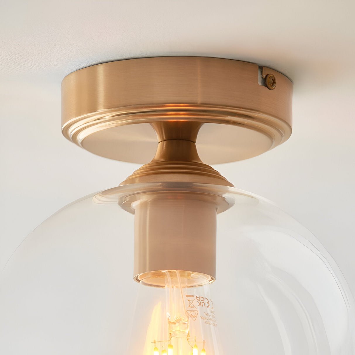 Halstead Flush Ceiling Light in aged brass with clear glass globe shade, close-up view showing E27 bulb and brass fitting detail.