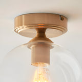 Halstead Flush Ceiling Light in aged brass with clear glass globe shade, close-up view showing E27 bulb and brass fitting detail.