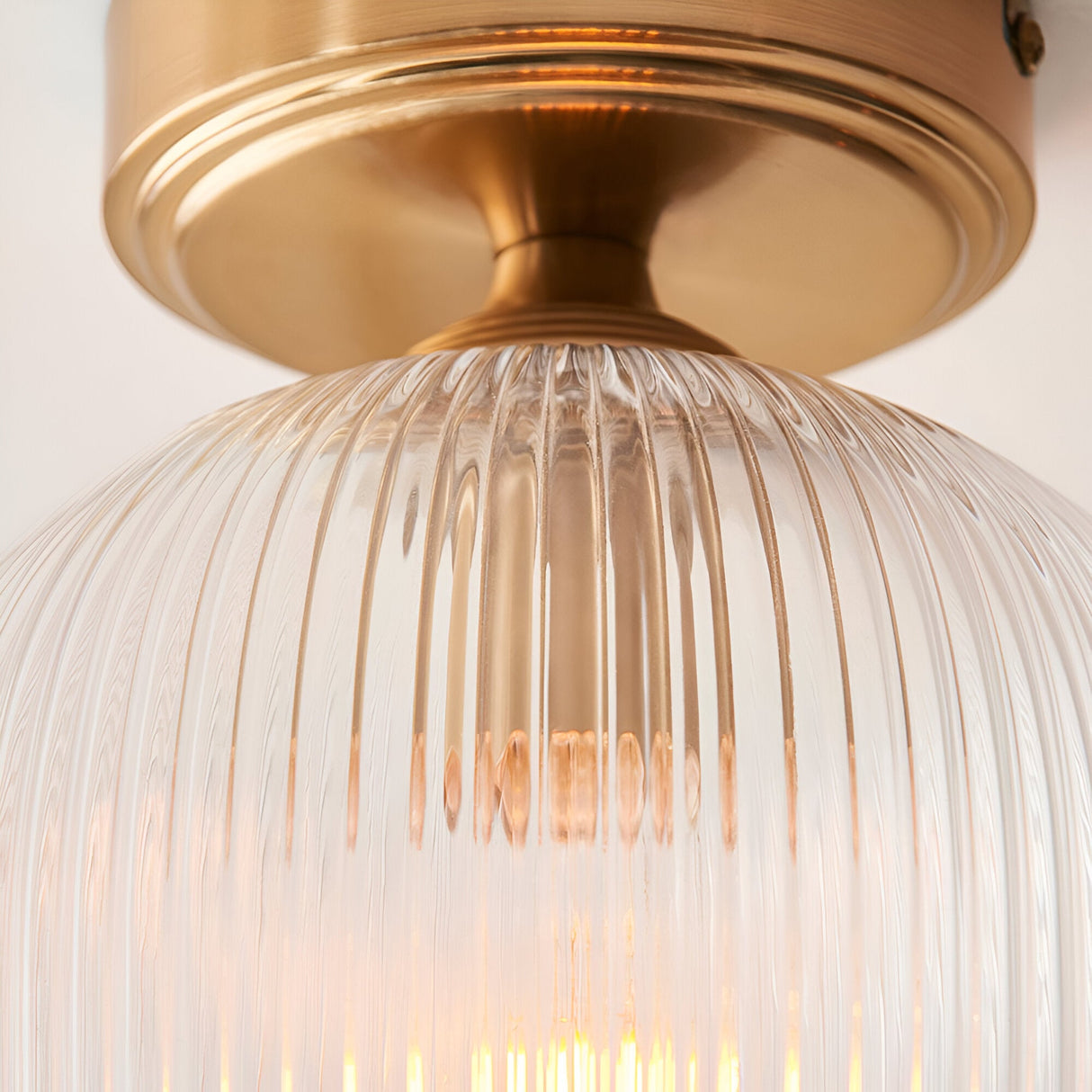 Close-up of the Endon Halstead flush ceiling light showing the aged brass fitting and ribbed clear glass shade with a glowing E27 lamp inside.