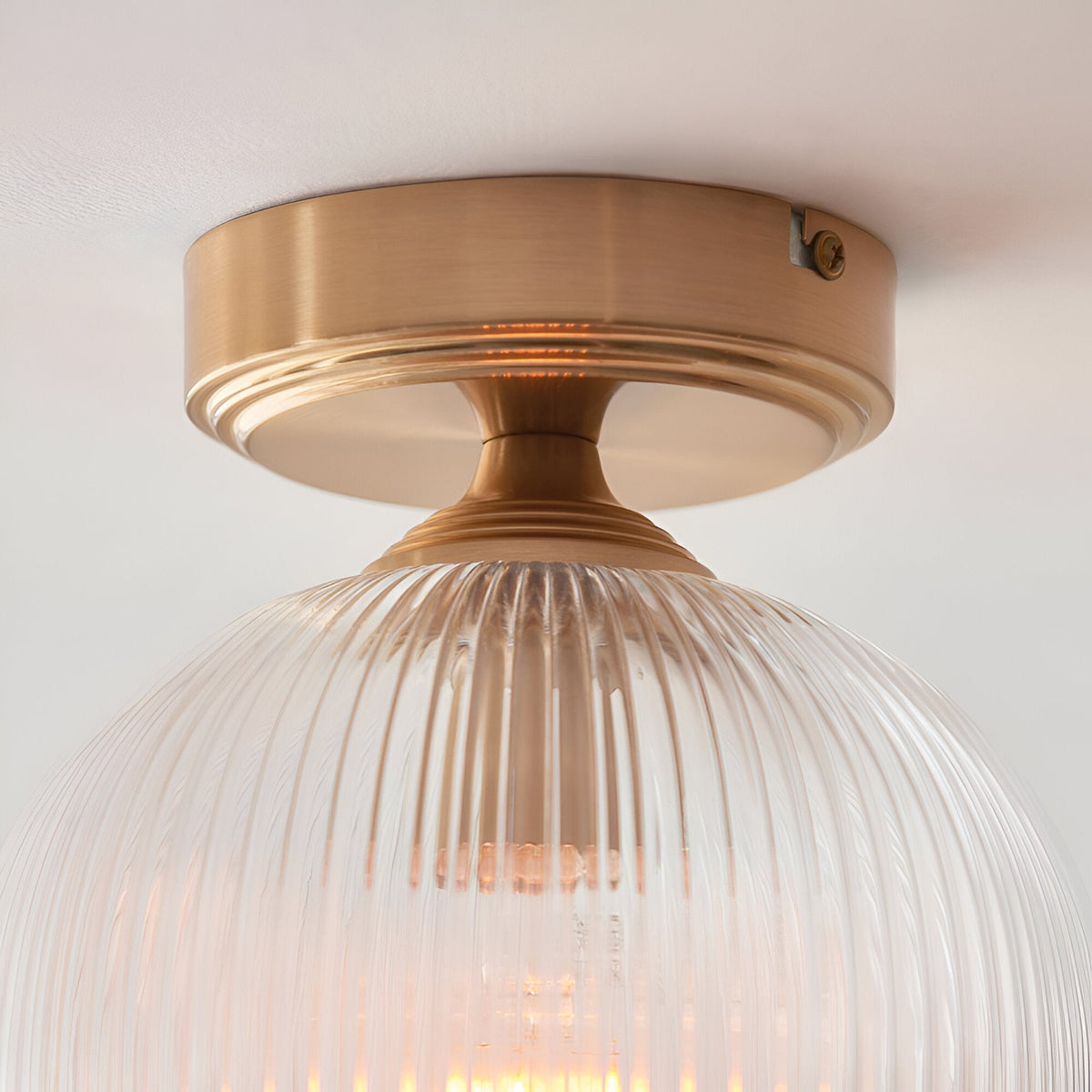 Endon Halstead flush ceiling light in aged brass with a ribbed clear glass globe shade, mounted close to a white ceiling.