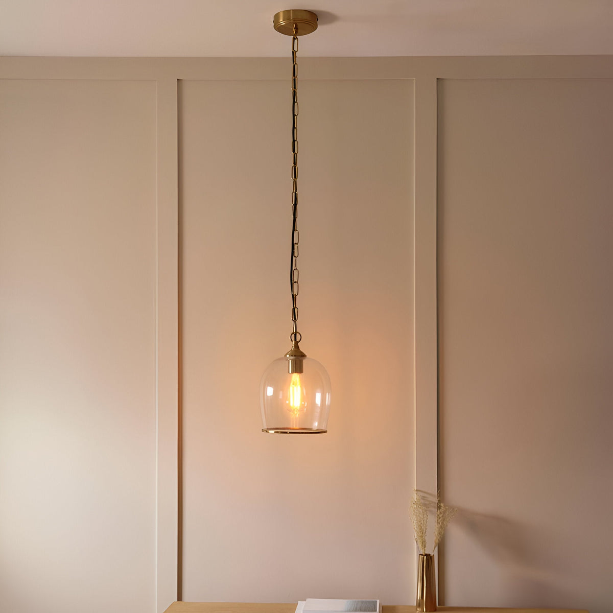 Halstead Pendant in brass with a clear glass dome shade and exposed bulb, hung on a chain in a softly lit dining room setting.