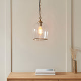 Halstead Pendant in brass, clear glass dome shade with brass edge and chain, hung above a wooden console with books and a vase.