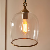 Halstead Pendant in brass with a clear glass dome shade, brass edge trim, chain suspension, and an exposed filament bulb, shown against a light background.