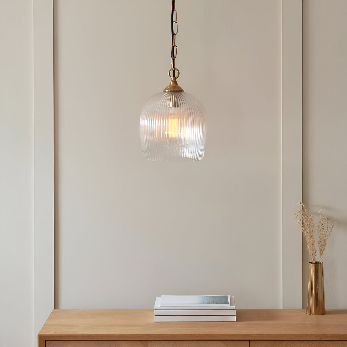 Endon Halstead ribbed pendant with fluted clear glass dome shade and brass chain, hung above a wooden console with books and a brass vase.