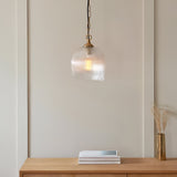 Endon Halstead ribbed pendant with fluted clear glass dome shade and brass chain, hung above a wooden console with books and a brass vase.