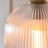 Close-up of the Endon Halstead Ribbed Pendant showing its fluted clear glass dome shade illuminated by a warm bulb, topped with a brushed brass fitting.