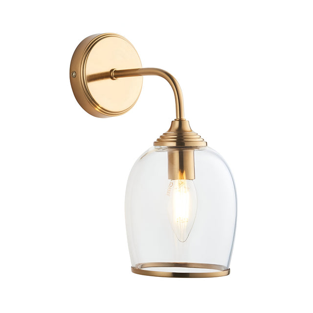 Halstead Wall Light in brushed brass finish, with a curved arm, round back plate, and clear domed glass shade housing an E14 bulb, shown on a white background.