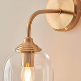 Halstead Wall Light in brushed brass finish, close-up of curved arm, round back plate and clear domed glass shade with visible E14 bulb.