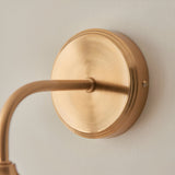 Close-up of the Halstead Wall Light in brass, showing the round backplate, curved arm, brushed antique brass finish, and fixing screw.